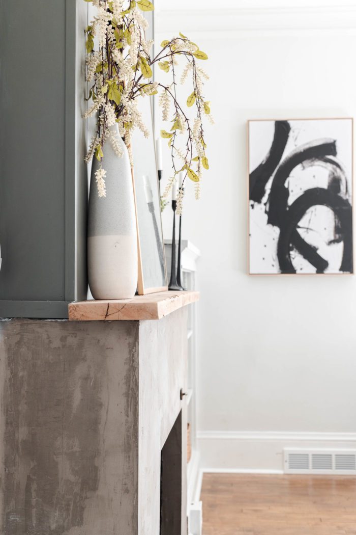 Floral stems in a tall vase sitting on a wooden mantel on a concrete fireplace. Spring Decor